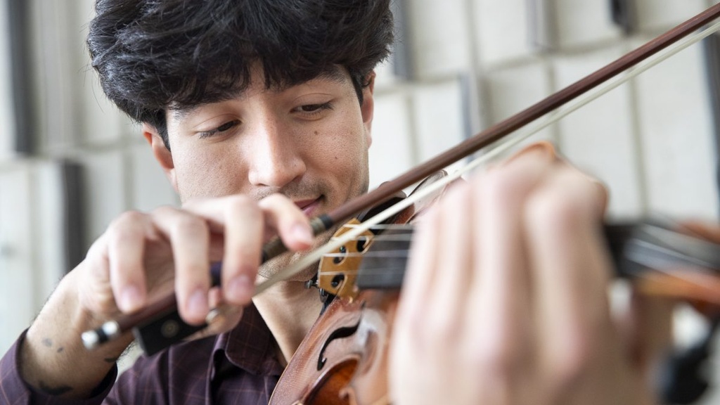 Oliver Bostain이 Voxman Music Building에서 바이올린을 들고 초상화를 위해 포즈를 취하고 있습니다.